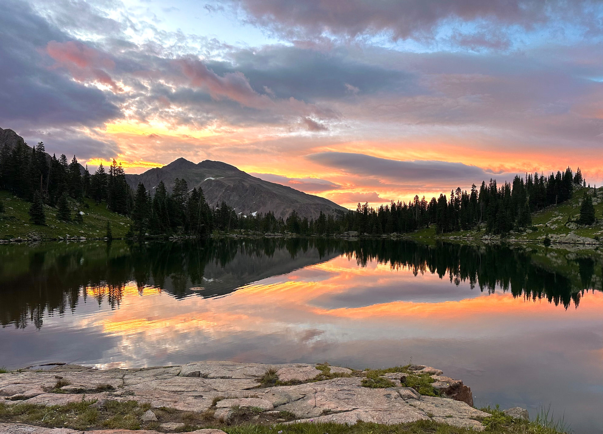 A mountain lake at sunset, mirrored in still water beneath a colorful sky