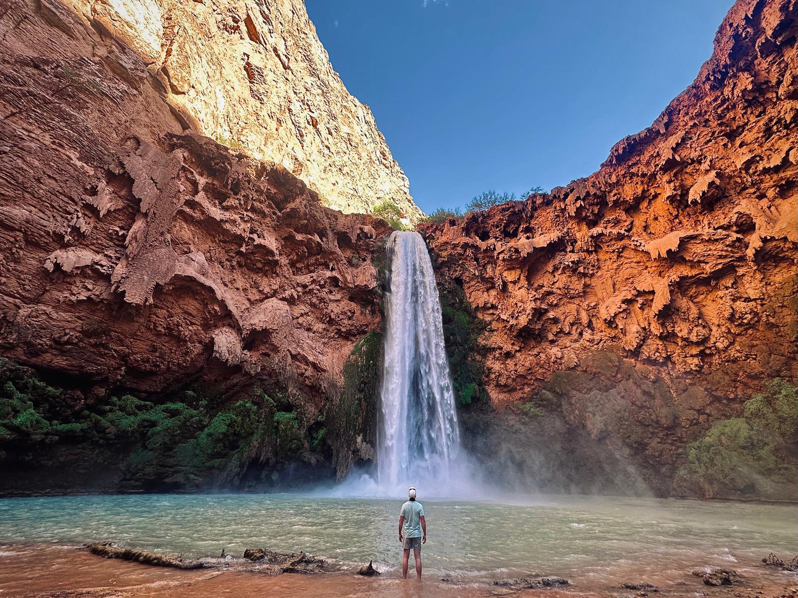 Nick McQueen standing in the water at the base of a tall canyon waterfall